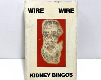 May include: A white album cover with the words "WIRE" and "KIDNEY BINGOS" in black text. A red square with a faded image of a face is in the center.