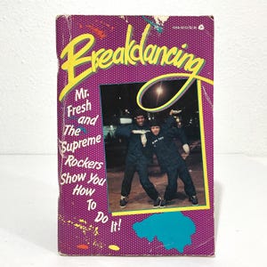 May include: A vintage paperback book titled Breakdancing: Mr. Fresh and The Supreme Rockers Show You How To Do It! The cover features a purple background with white polka dots and a central photograph of two dancers in dark jackets and white gloves.