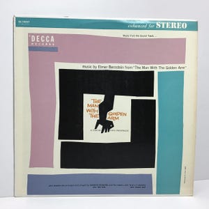May include: A vintage vinyl record album cover for "The Man With The Golden Arm." The design features a black and white graphic of a hand and arm, with the title text in white. The album cover has a retro color scheme with pink, blue, and cream tones.