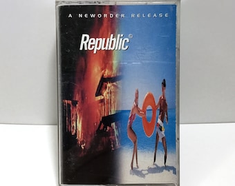 Puede incluir: Una cinta de casete de New Order con una imagen de fuego rojo, naranja y amarillo en el lado izquierdo y una imagen de cielo azul y océano en el lado derecho. La cinta de casete tiene el texto "Republic" en letras blancas sobre fondo negro.