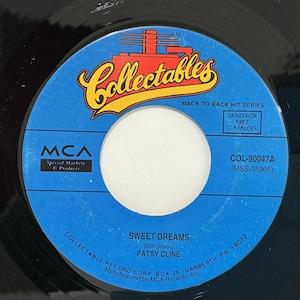 May include: A black vinyl 45 RPM record with a blue center label. The label features the Collectables logo in yellow and red, the text "BACK TO BACK HIT SERIES," "SWEET DREAMS," "PATSY CLINE," "MCA," and "COL-90047A" printed in black ink.