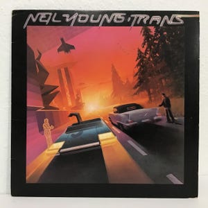 May include: Album cover for Neil Young's "Trans." The artwork features a futuristic cityscape with a car, a person, and a jet. The sky is a gradient of orange and pink. The album title is at the top.