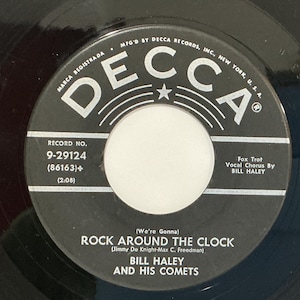 May include: A black vinyl record label with white text. The Decca logo is at the top. The text reads: (We're Gonna) ROCK AROUND THE CLOCK, BILL HALEY AND HIS COMETS, RECORD NO. 9-29124, (86163), (2:08), Fox Trot, Vocal Chorus By BILL HALEY.