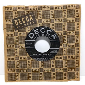 May include: A vintage 45 RPM vinyl record titled Basin Street Blues Part 1 by Louis Armstrong and the All Stars, featuring a black center label with white text, housed in a tan paper sleeve with a repeating brown Decca Records logo pattern.