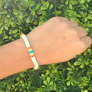 May include: A white beaded bracelet with a colorful stripe of orange, yellow, blue, and green beads.