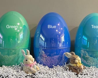 May include: Five large plastic Easter eggs in different colours: pink, green, blue, teal, and purple. Each egg has a label with its colour name.