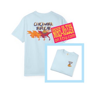 May include: Light blue t-shirt with a graphic featuring a dinosaur and the text "CLOCKWORK TRIPLICATE". A pink sticker reads "BEER IS THE MIND-KILLER on Etsy.com". A smaller image shows the shirt with a small graphic.