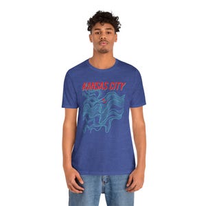 May include: A royal blue t-shirt with a blue and red graphic design. The graphic design features a stylized wave pattern with the text "KANSAS CITY" in red.