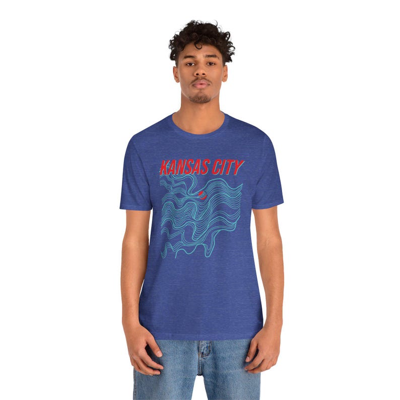 May include: A royal blue t-shirt with a blue and red graphic design. The graphic design features a stylized wave pattern with the text "KANSAS CITY" in red.