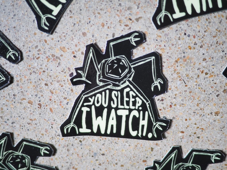 May include: Black and white sticker with a robot-like creature with the text "You sleep. I watch."