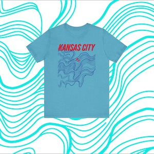 May include: A light blue t-shirt with a graphic design of blue and red wavy lines. The text "KANSAS CITY" is printed in red on the shirt.