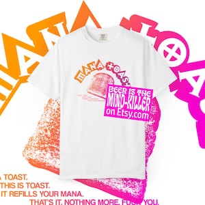 Op de afbeelding: Een wit t-shirt met korte mouwen en een afbeelding van een geroosterde boterham met de tekst MANA TOAST erboven. Onder de toast staat in kleinere letters MANA TOAST. THIS IS TOAST. IT REFILLS YOUR MANA. THAT'S IT. NOTHING MORE. Een roze kader ligt eroverheen.