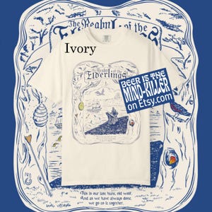 May include: Ivory-colored t-shirt with a detailed graphic featuring a ship, figures, and text that reads "The Realm of the Elderlings." A blue square with "BEER IS THE MIND-KILLER on Etsy.com" is also visible.