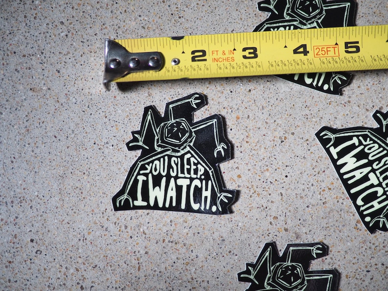 May include: Black and white sticker with a robot-like creature and the text "You sleep. I watch."