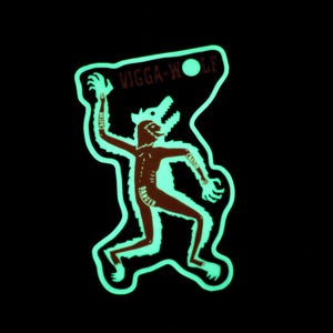 May include: A sticker with a brown werewolf-like figure with a glowing green outline. The text "WIGGA-WOLF" is above the figure. The word "CAUTION" is on the figure's arm. The background is black.