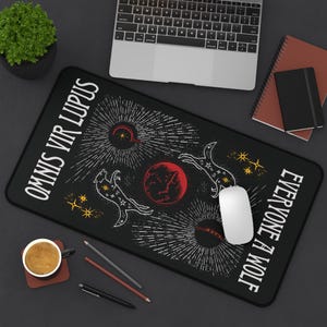 May include: Black rectangular mouse mat featuring a celestial wolf design. The design includes a red planet, white wolves, and the text "OMNIS VIR LUPUS" and "EVERYONE A WOLF" in white. A white mouse sits on the mat.