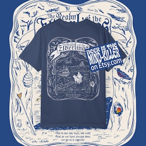 May include: Navy blue t-shirt featuring a detailed white illustration with the text "The Realm of the Elderling." The design includes a ship, figures, and a mountain scene. Additional text on the shirt reads "BEER IS THE MIND-KILLER on Etsy.com."