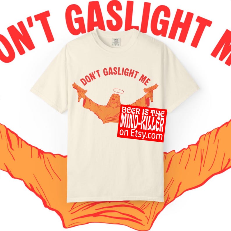 May include: Cream-colored t-shirt with the phrase "DON'T GASLIGHT ME" in red. The shirt features an orange graphic of a figure with a halo holding two guns. A red square with the text "BEER IS THE MIND-KILLER on Etsy.com" is also visible.