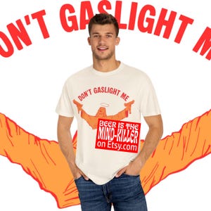May include: Cream-colored t-shirt with the text "DON'T GASLIGHT ME" in red. The shirt features an orange graphic of a figure with outstretched arms and a halo, and the text "BEER IS THE MIND-KILLER on Etsy.com" in a red box.