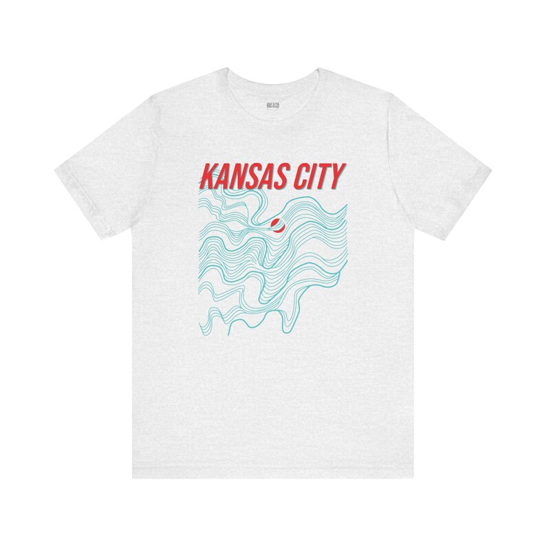 May include: A heather grey t-shirt with a graphic design of blue wavy lines and the text "KANSAS CITY" in red.