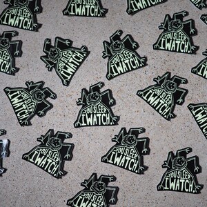 May include: A collection of black and white stickers with a glow-in-the-dark design. The stickers feature a cartoon creature with the text "You Sleep I Watch."