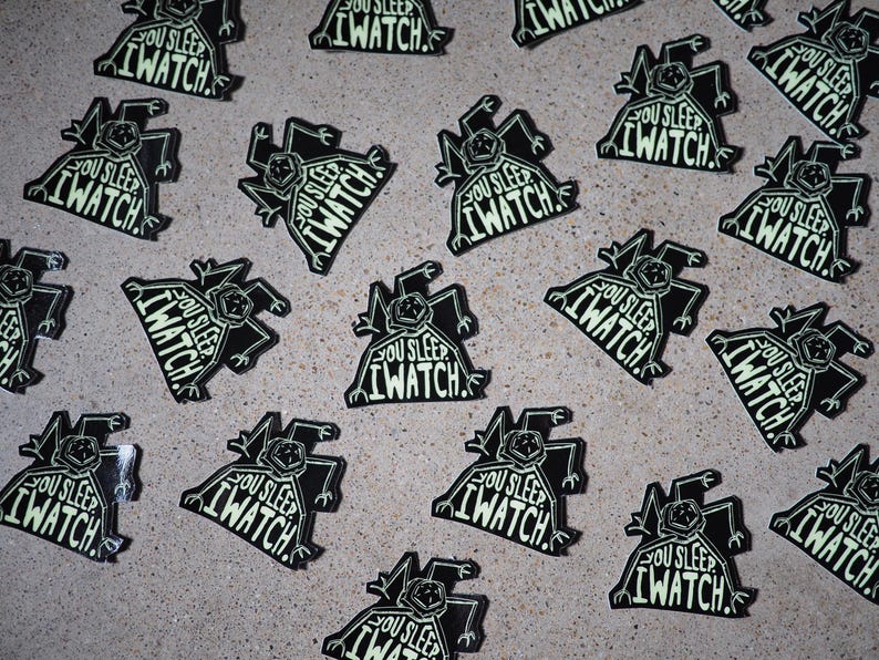 May include: A collection of black and white stickers with a glow-in-the-dark design. The stickers feature a cartoon creature with the text "You Sleep I Watch."