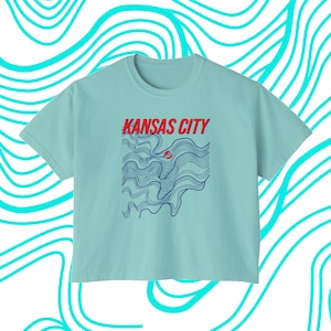 May include: A light blue t-shirt with a graphic design of blue wavy lines and the text "KANSAS CITY" in red and blue letters.