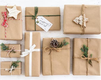 May include: An overhead shot of several wrapped gifts in brown paper, decorated with twine, ribbons, and festive accents. Some gifts feature wooden star and tree ornaments, while others have sprigs of greenery and pinecones. One gift has a tag that says "Merry Christmas."