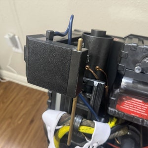 May include: A black and gray plastic device with a metal rod extending from the top. The device has a red warning label with text that is partially visible. The device is connected to wires and other components.