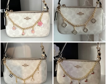 Puede incluir: Cuatro bolsos Coach blancos con cadenas doradas y abalorios. Los abalorios incluyen flores, corazones, llaves, cerezas y tréboles.