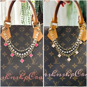 May include: A brown handbag with a gold chain and pink clover charms. The handbag has brown leather handles and gold hardware. The chain is layered with white pearls and gold links.