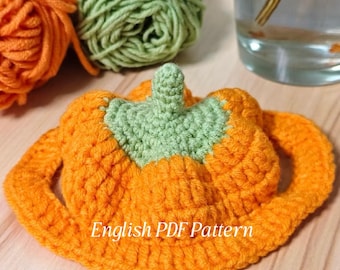 May include: An orange and green crocheted pumpkin with the text "English PDF Pattern". The pumpkin has a green stem and a circular brim. Two balls of yarn, one orange and one green, are in the background.