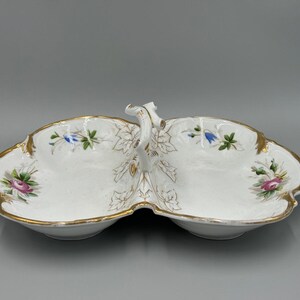 May include: A white, divided serving dish with a gold trim and handle. The dish is decorated with floral and leaf patterns in pink, blue, and green. The dish is approximately 10 inches long.