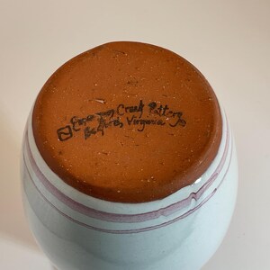 Puede incluir: Un jarr&oacute;n de cer&aacute;mica blanco con un esmalte azul claro y rayas rosas. La base del jarr&oacute;n es marr&oacute;n y tiene el texto "Etowah Craft Pottery, Bedford, Virginia" estampado.
