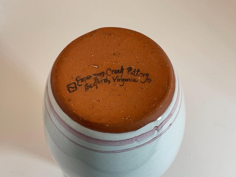 Puede incluir: Un jarr&oacute;n de cer&aacute;mica blanco con un esmalte azul claro y rayas rosas. La base del jarr&oacute;n es marr&oacute;n y tiene el texto "Etowah Craft Pottery, Bedford, Virginia" estampado.