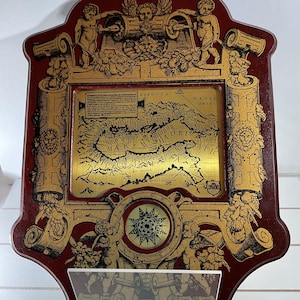May include: A red and gold framed map of the Adriatic Sea with the text "MARE ADRIATICUM" in gold lettering. The map is surrounded by a decorative border with cherubs and scrolls. The frame is made of wood and has a distressed finish.