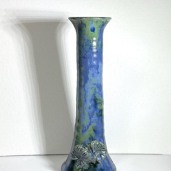Peut inclure: Un vase en céramique de grande taille, avec un sommet évasé et une surface texturée. Le vase est principalement bleu avec des touches de vert et un motif de feuilles décoratives près de la base. Le vase mesure environ 30 cm de haut.