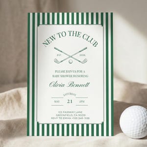 Close-up of a green striped baby shower invitation standing on soft fabric, accented with a white golf ball to emphasize the golf club themed design.