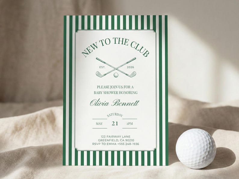 Close-up of a green striped baby shower invitation standing on soft fabric, accented with a white golf ball to emphasize the golf club themed design.