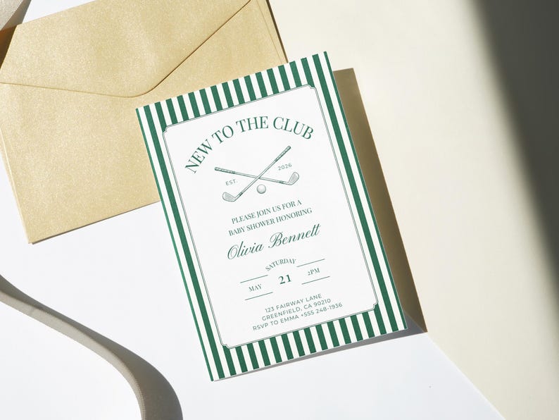 Printable baby shower invitation with green striped border displayed upright on soft linen fabric, styled with a white golf ball and wooden tees for a classic country club look.
