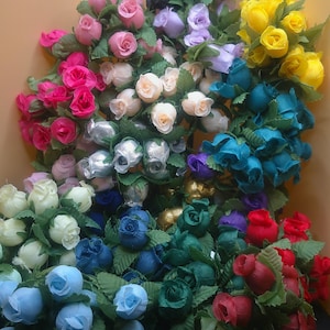 May include: Assortment of artificial rose buds in various colors, including white, pink, red, blue, green, yellow, and black. The rose buds are arranged in a bouquet and are perfect for crafting or decorating.