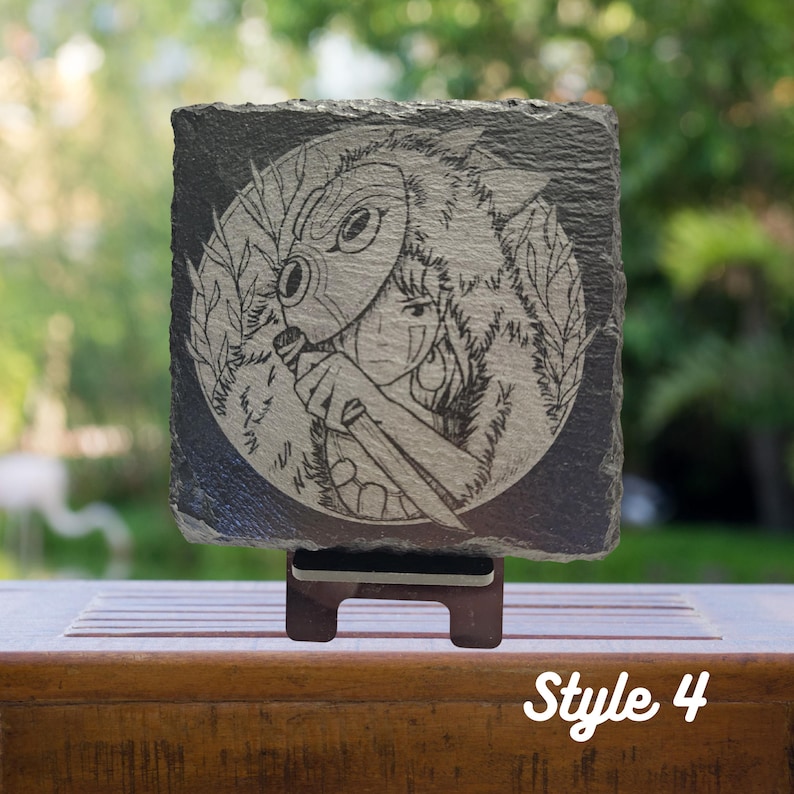 May include: A black and white engraved image of a character from the animated film "Princess Mononoke" on a slate coaster. The character is wearing a wolf mask and holding a sword. The coaster is on a wooden stand.