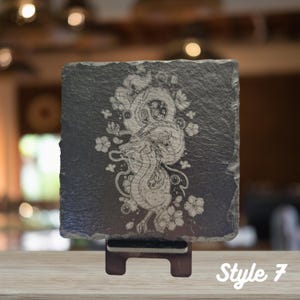 May include: A black slate coaster with a white engraved design of a dragon with floral accents. The coaster is on a stand and the text "Style 7" is visible in the bottom right corner.