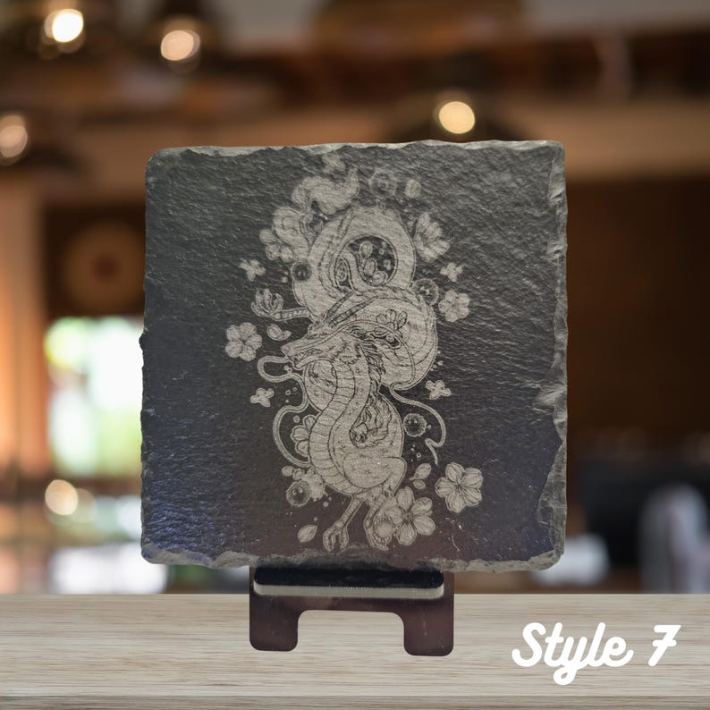 May include: A black slate coaster with a white engraved design of a dragon with floral accents. The coaster is on a stand and the text "Style 7" is visible in the bottom right corner.
