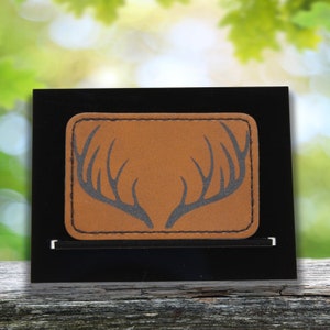 Puede incluir: Un parche de cuero marrón con una silueta negra de una cornamenta de ciervo.