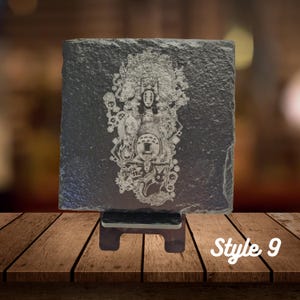 May include: A black slate coaster with a white engraved image of characters from the animated film Spirited Away. The coaster is on a wooden stand. Style 9.