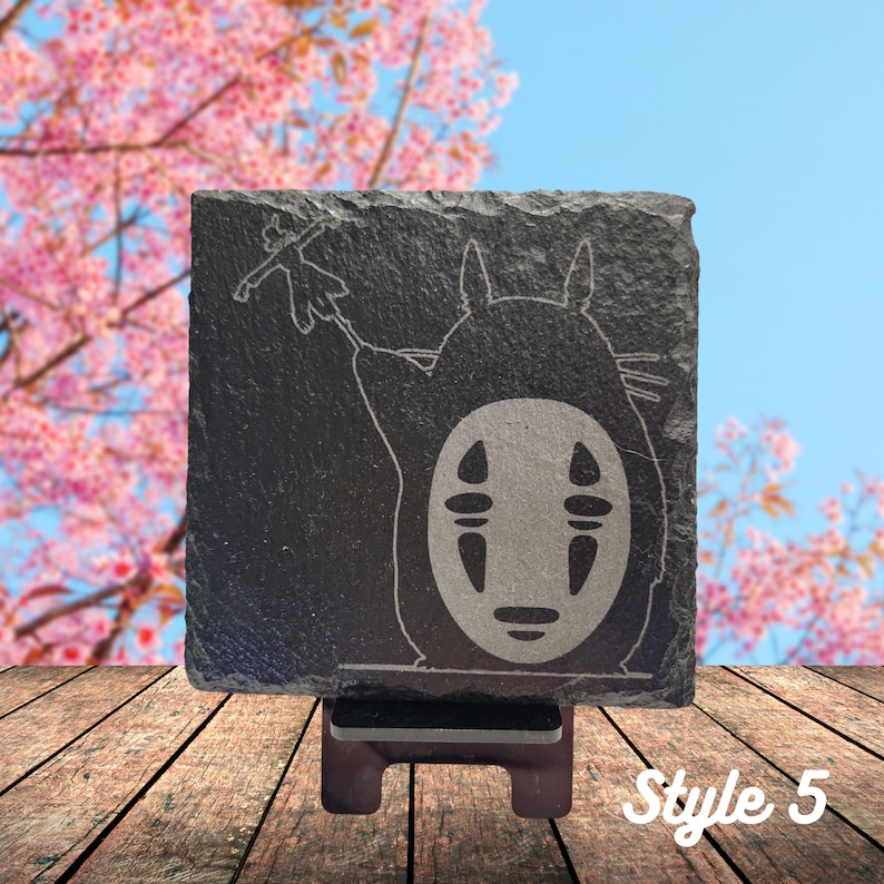 May include: A black slate coaster with a white engraved image of No Face from the movie Spirited Away. The coaster is on a wooden stand. Style 5.