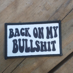 Puede incluir: Un parche blanco con texto negro que dice "Back on my Bullshit".