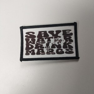 May include: A black and white patch with the text "Save Water Drink Margs" in a retro font.