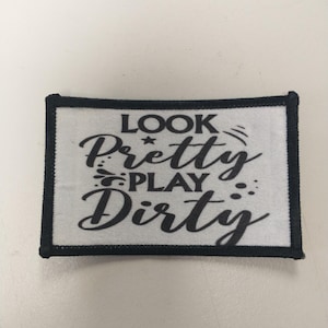 May include: Black and white embroidered patch with the text "Look Pretty Play Dirty" on a white background.